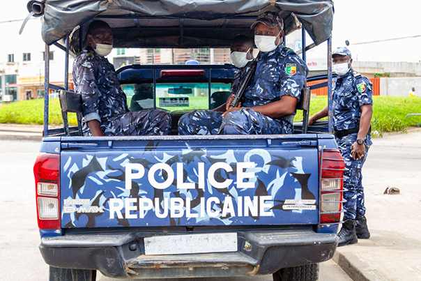 Quatre policiers en uniforme et masque de protection sur et autour d un véhicule marqué Police Républicaine