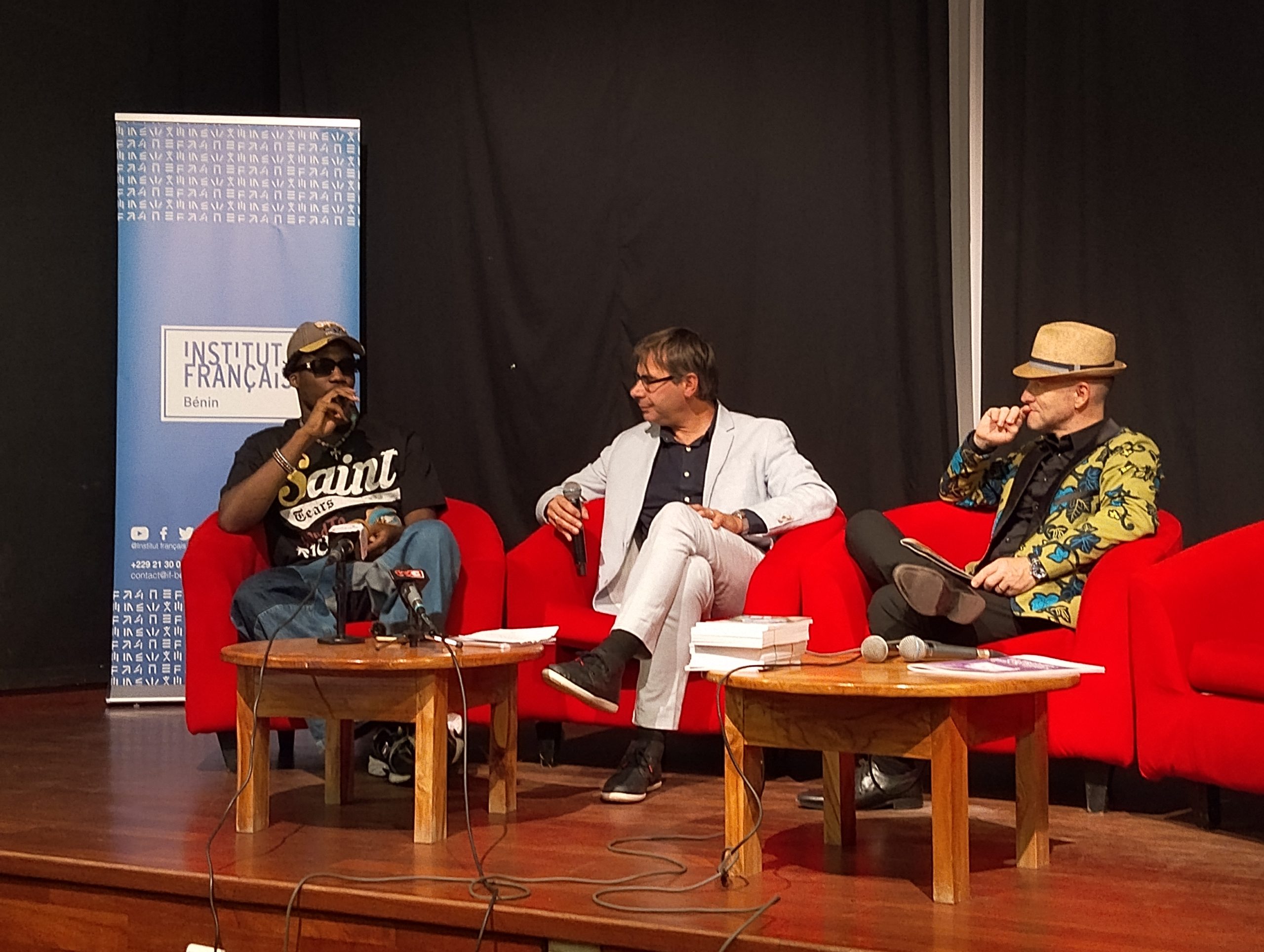 Trois hommes assis sur des fauteuils rouges participent à une discussion sur scène devant une bannière Institut Français