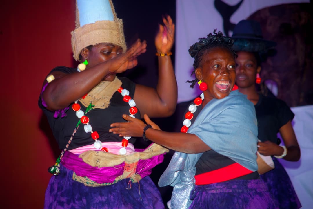 Trois femmes dansent en tenue colorée et joyeuse dans un décor sombre avec des accessoires traditionnels