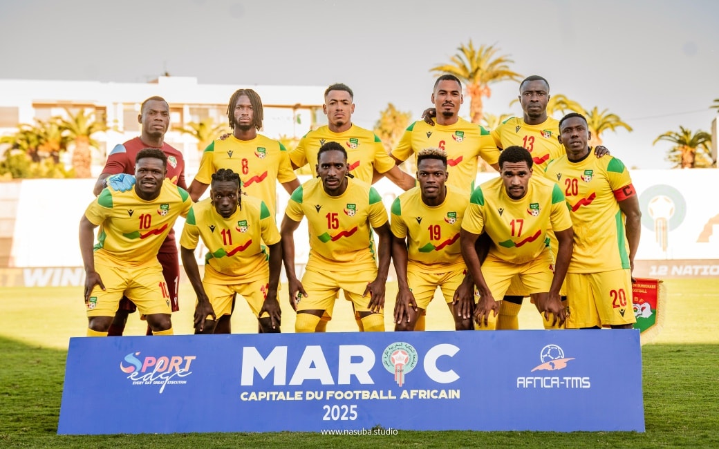Onze joueurs vêtus de maillots jaunes posant sur un terrain de football derrière une banderole bleu avec plusieurs logos et « MAROC 2025
