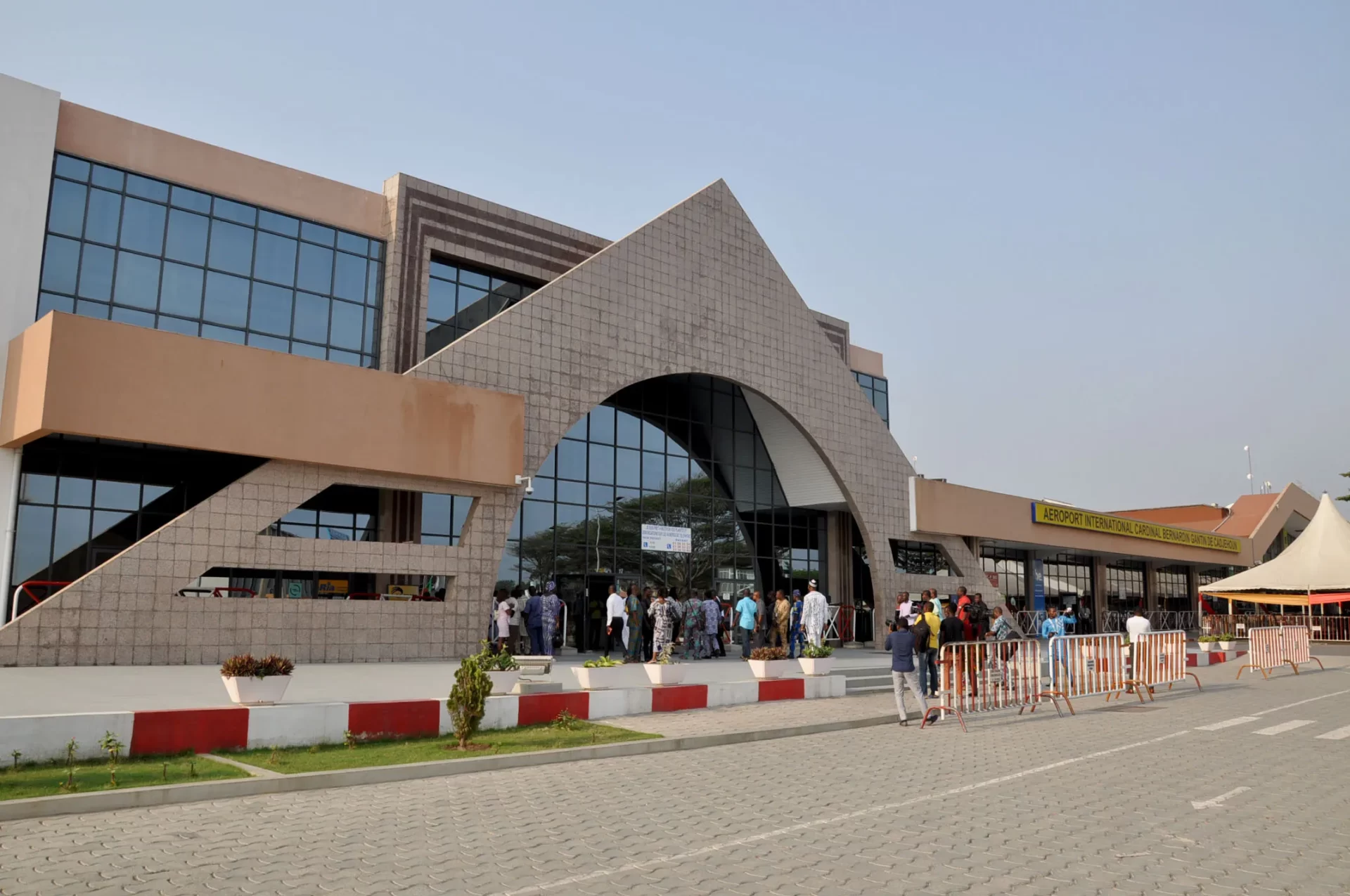 Façade d un terminal d aéroport moderne avec une foule de personnes à l entrée et un grand panneau jaune visible sur le bâtiment