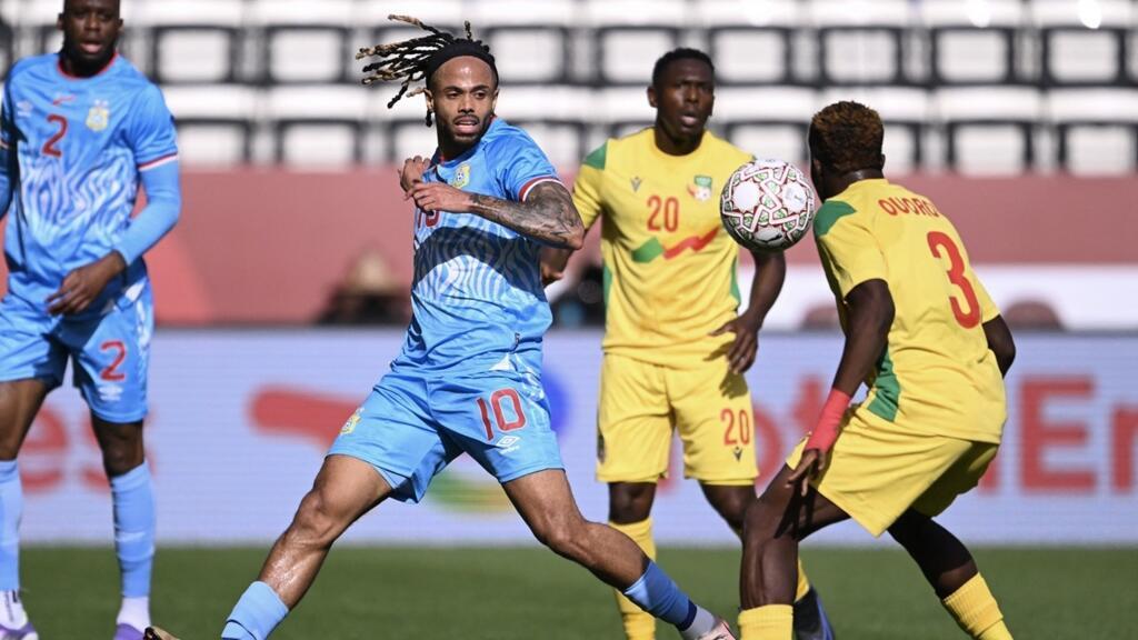 Un joueur en maillot bleu contrôle le ballon face à deux adversaires en maillots jaunes sur un terrain de football