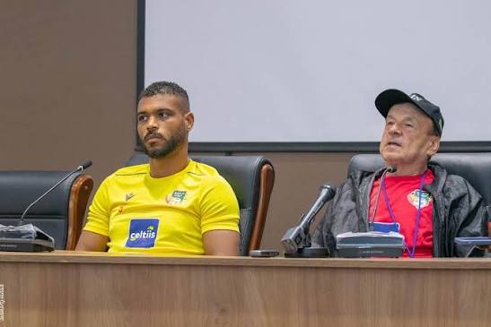 Deux hommes assis à une table de conférence avec un micro et un écran blanc en arrière-plan