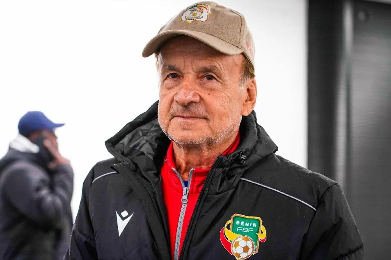 Homme âgé en veste noire avec blason d'équipe de football portant une casquette beige regardant devant lui avec sérieux