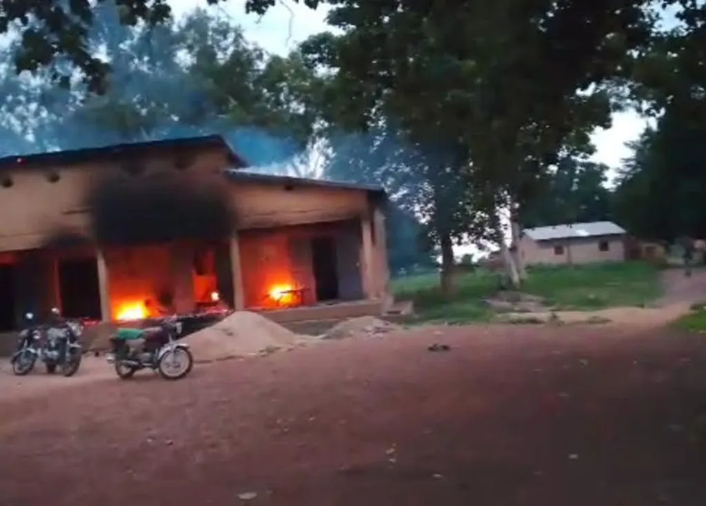 Bâtiment en feu avec de la fumée noire, deux motos garées devant, arbres autour et ciel en fin de journée