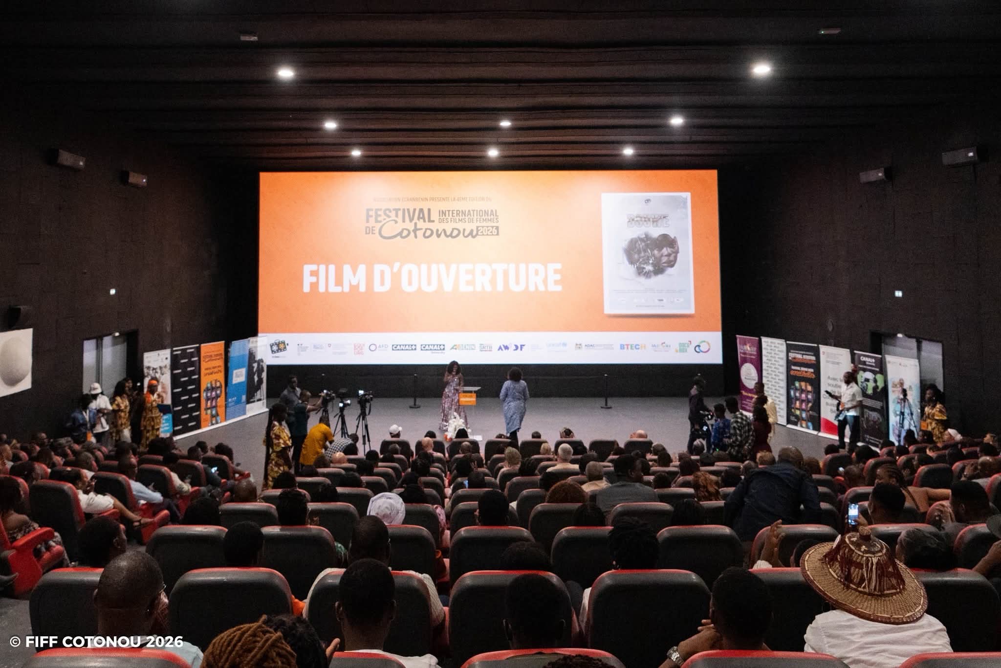 Salle de cinéma remplie avec deux personnes sur scène devant un écran affichant Film d'ouverture