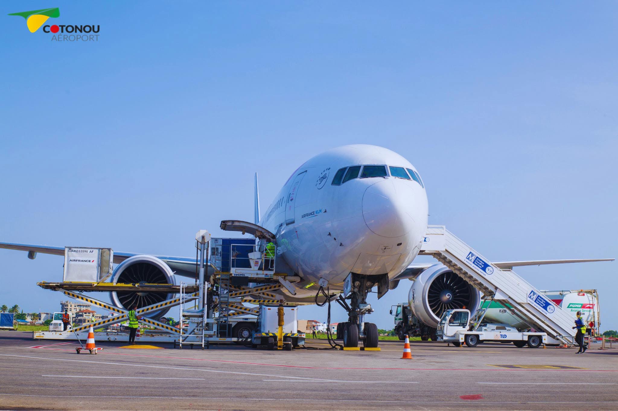 Un avion stationné sur le tarmac avec plusieurs équipements de chargement et du personnel autour sous un ciel bleu clair