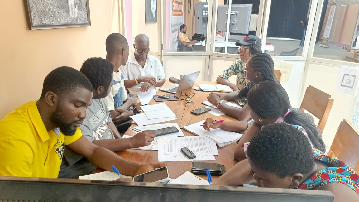 Plusieurs personnes assises autour d’une table en bois en réunion avec documents et ordinateurs portables.