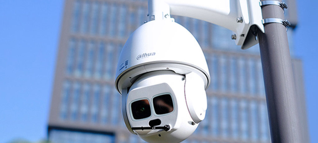Caméra de surveillance montée sur un poteau sous un ciel bleu avec un bâtiment flou en arrière-plan