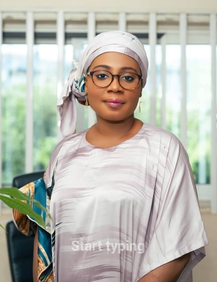 Femme portant un foulard et des lunettes posant devant une fenêtre lumineuse dans une pièce intérieure