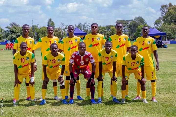 Onze jeunes joueurs de football en tenue jaune et verte posent sur un terrain herbeux sous un ciel partiellement nuageux