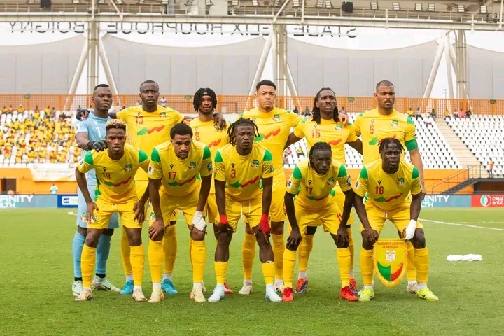Onze joueurs de football posent sur le terrain, vêtus de maillots jaunes avec des détails verts et rouges, en formation pour une photo d'équipe
