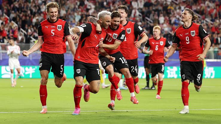 Des joueurs en maillot rouge et noir célèbrent un but sur un terrain de football devant un public nombreux