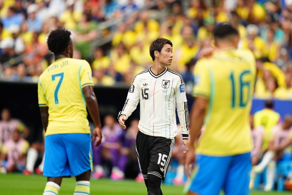 Trois joueurs de football dont deux en maillots jaunes et un en maillot blanc discutent sur le terrain pendant un match