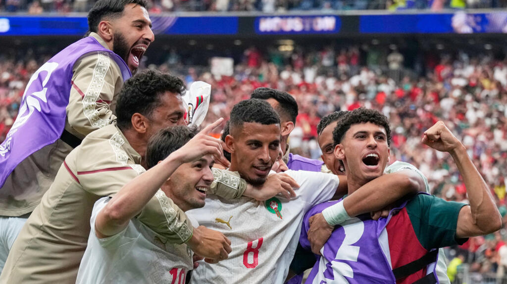 Groupe de joueurs de football en maillots blancs célébrant joyeusement un but dans un stade rempli de supporters