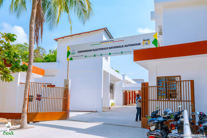Entrée d’un bâtiment blanc avec un panneau « Commission Électorale Nationale Autonome » et plusieurs motos garées à droite