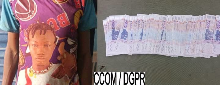 Un homme tenant un faux billet à côté d'une rangée de billets de banque de 1000 FCFA posés sur une surface grise