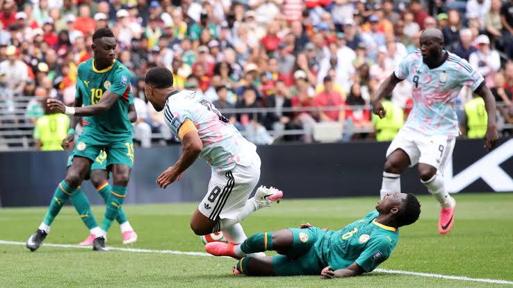 Deux joueurs en maillot vert tentent un tacle face à deux joueurs en maillot blanc sur un terrain de football bondé